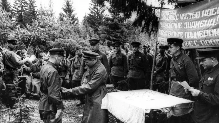 Северо-Западный фронт. Вручение ордена Красного Знамени гвардии младшему лейтенанту Павлу Тулянкину. Надпись на транспаранте: «Гвардейцы, с честью носите гвардейские знамена! Всегда будьте примером доблести и отваги в борьбе с врагом!». Август 1942 г. Фото: Серей Коршунов/МАММ/МДФ/russiainphoto.ru
